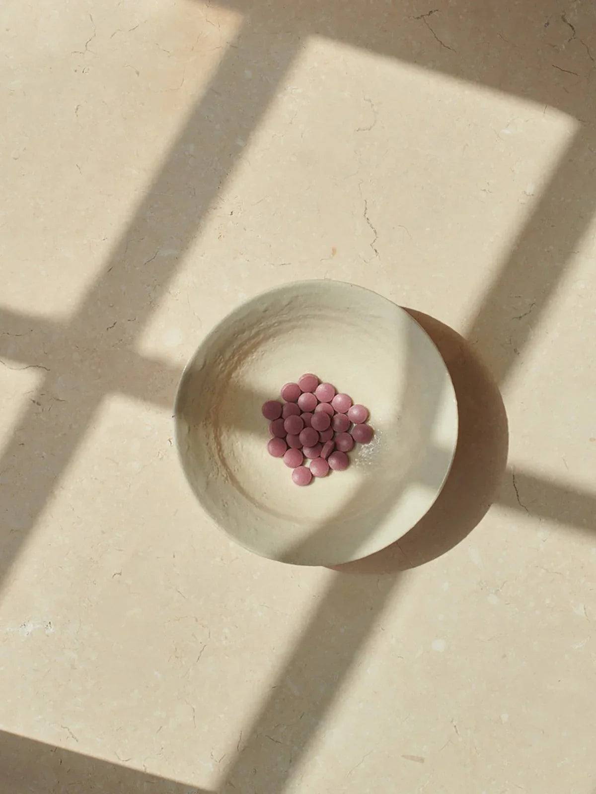 Lyserøde kapsler i en rund, lys keramikskål på en neutral, lys overflade med naturligt lys fra et vindue, der fremhæver. - Jern Organisk (90 stk.)