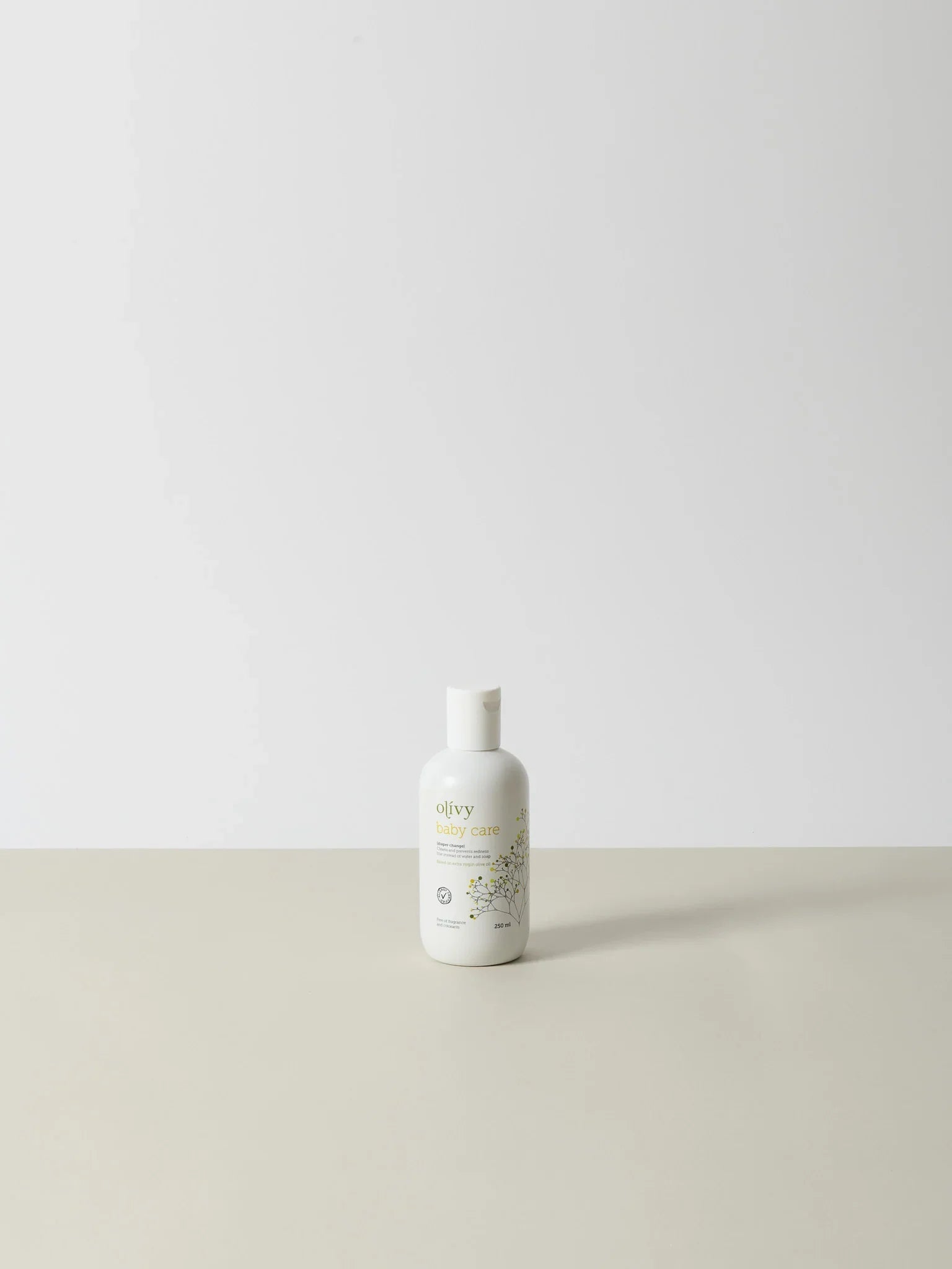 Hvid flaske med naturlig, nænsomt formuleret Olivy olie, premium kvalitet, 250 ml, stående på beige overflade mod lys. - Olivy (250ml)